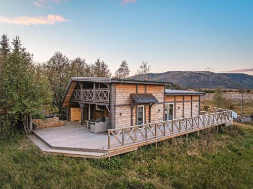 a wooden house with a large deck in a field at Riverside Cabin - Hot Tub, Fishing and Relaxing Escape in Laugarvatn