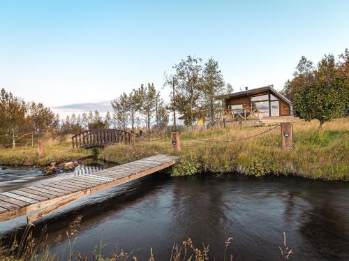 a house on a hill with a bridge over a river at Riverside Cabin - Hot Tub, Fishing and Relaxing Escape in Laugarvatn