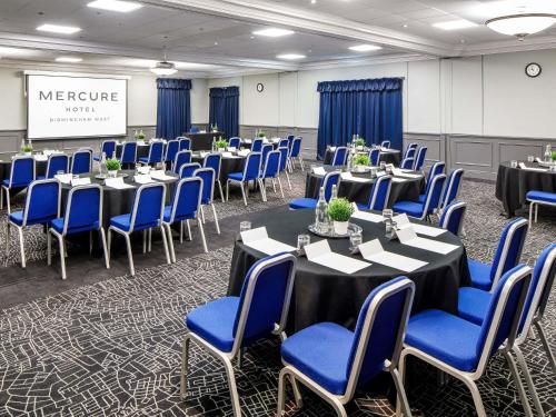 a conference room with tables and blue chairs at Mercure Birmingham West Hotel in West Bromwich