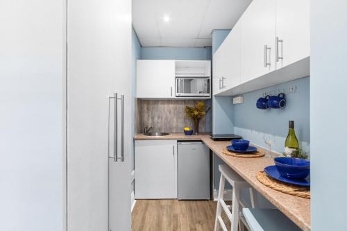 cocina con armarios blancos y paredes azules en Eden On The Bay 67A by Host Agents, en Big Bay