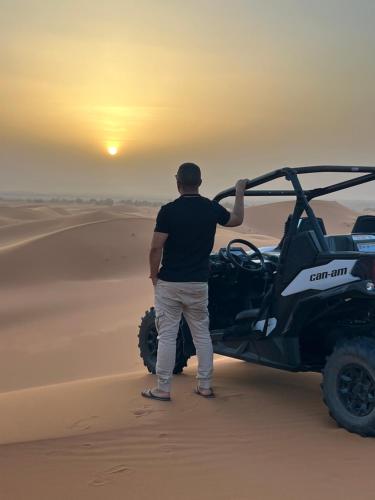 a man standing next to a vehicle in the desert at Sahara Majestic Luxury Camp in Merzouga