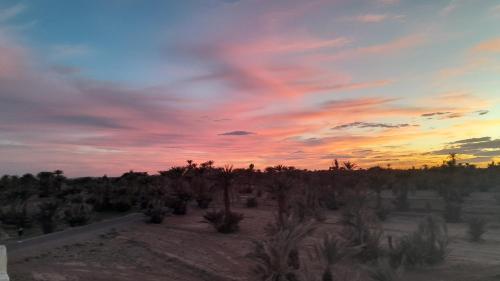 a sunset in the desert with palm trees at Mhamid Auberge Saharaespace in Mhamid