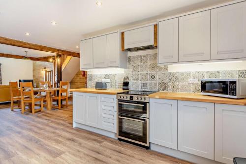 a kitchen with white cabinets and a dining room at Monks Barn in Upwell
