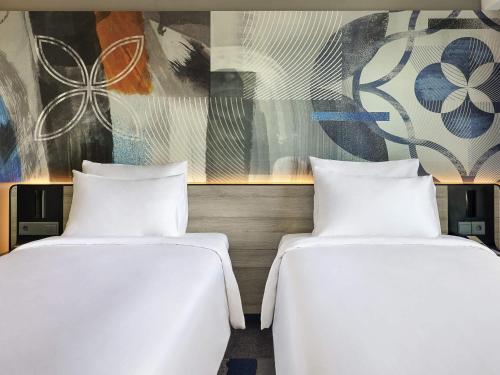 two white beds in a room with a painting at Novotel Suites Yogyakarta Malioboro in Yogyakarta