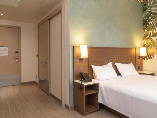 a hotel room with a bed and a telephone at ibis Styles Curitiba Aeroporto in São José dos Pinhais