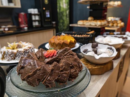 a table topped with different types of cakes and desserts at ibis Styles Curitiba Aeroporto in São José dos Pinhais