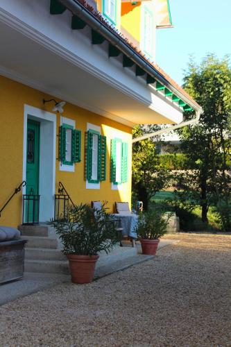 a yellow house with green shuttered windows and potted plants at Burgunderhof - Steiermark in Sankt Anna am Aigen
