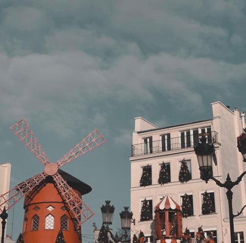 Un molino de viento naranja frente a un edificio. en Architect Studio Moulin Rouge, en París