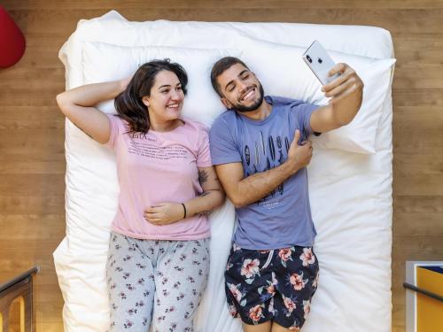 a man and a woman laying on a bed with a cell phone at ibis budget Sao Caetano in São Caetano do Sul