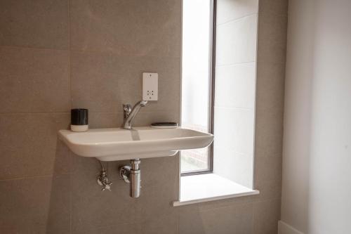 Un lavabo blanco en un baño con ventana. en Rookery Park Barns 6, en Carlton Colville