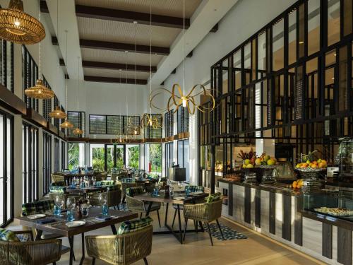 a restaurant with tables and chairs in a room with windows at Pullman Maldives Maamutaa - All-Inclusive Resort - 50 percent off Transfers in Maamutaa