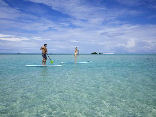 two people are standing on surfboards in the ocean at Pullman Maldives Maamutaa - All-Inclusive Resort - 50 percent off Transfers in Maamutaa