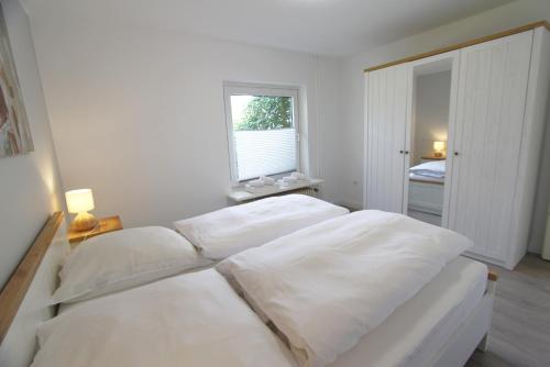 a white bedroom with two beds and a window at Denghoog- Osetal 10, App 2 in Wenningstedt