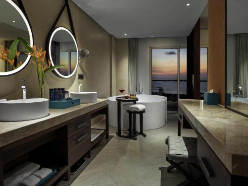 a bathroom with two sinks and a tub and mirrors at Pullman Phu Quoc Beach Resort in Phu Quoc