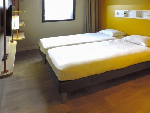 two beds in a room with yellow walls and wooden floors at Ibis Budget Perigueux Boulazac in Boulazac