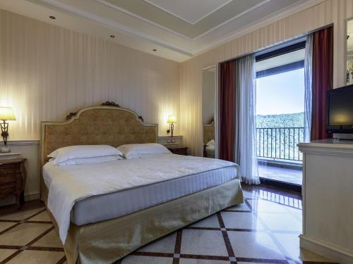 a bedroom with a large bed and a large window at Mercure Petriolo Siena Terme Spa Hotel in Bagni di Petriolo