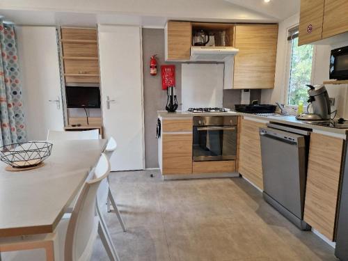 a kitchen with wooden cabinets and a table with chairs at MH3-Confort, 3ch, 6 pl, 2 FUN-PASS OFFERT dès 5 nuits, LAVE VAISSELLE, TV, WI-FI, Draps fournis et ménage, en option ! in Pont-Aven