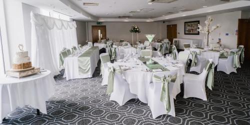 a banquet room with white tables and chairs with white bows at voco St. David's Cardiff by IHG in Cardiff