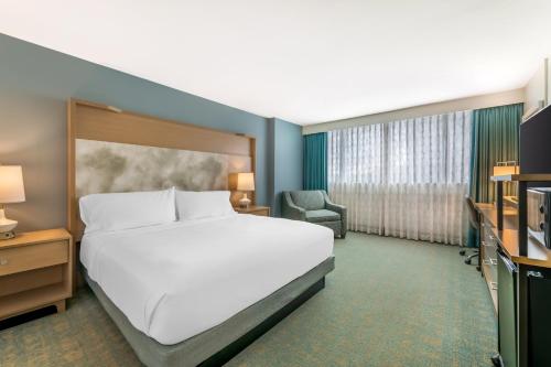 a bedroom with a large white bed and a chair at Holiday Inn Orlando – Disney Springs® Area by IHG in Orlando