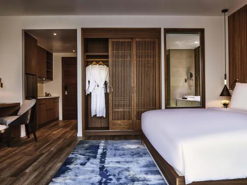 a bedroom with a white bed and a kitchen at Mövenpick Villas & Residences Phu Quoc in Phu Quoc