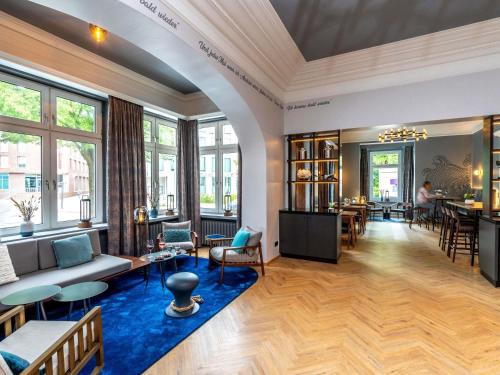 a living room with a couch and tables and windows at Mercure Hotel Luebeck City Center in Lübeck