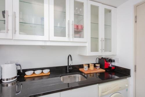 a kitchen with white cabinets and a sink at Stylish 1 Bedroom Apartment Near Northcote Road in London