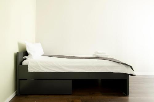 a bed in a bedroom with a white wall at Olive Stays Apartment - 2 in Pristina