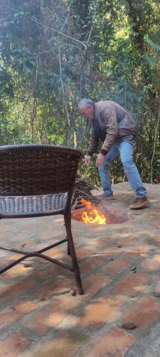 a man standing over a fire next to a bench at Cabana Rústica da Natureza in Jundiaí