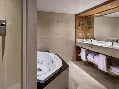 a bathroom with a tub and two sinks and a mirror at Mövenpick Hotel Lausanne in Lausanne