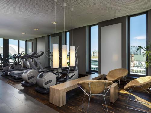 a gym with treadmills and exercise equipment and windows at Mövenpick Hotel Frankfurt City Messe in Frankfurt/Main