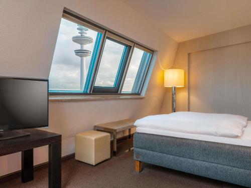 a bedroom with a bed and a tv and a window at Mövenpick Hotel Hamburg City in Hamburg