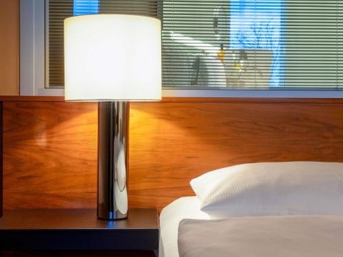 a lamp sitting on a table next to a bed at Mövenpick Hotel Hamburg City in Hamburg