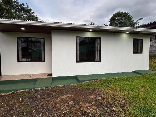 a white house with two windows and a yard at Sonrisas del Arenal La Fortuna in Chachagua