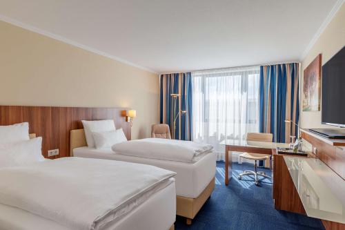a hotel room with two beds and a desk at NH Ingolstadt in Ingolstadt