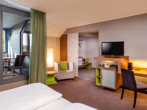 a hotel room with a bed and a flat screen tv at Mövenpick Hotel München-Airport in Hallbergmoos