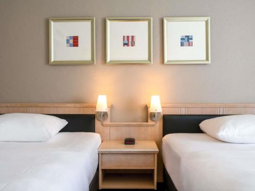 two beds in a room with three pictures on the wall at Mövenpick Hotel München-Airport in Hallbergmoos