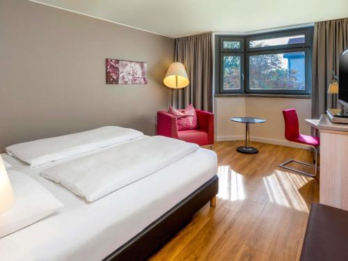 a bedroom with a bed and two red chairs at Mövenpick Hotel München-Airport in Hallbergmoos