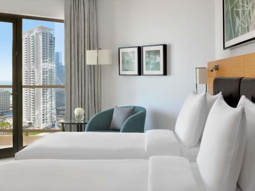a hotel room with a white bed and a chair at Mövenpick Hotel Jumeirah Beach in Dubai