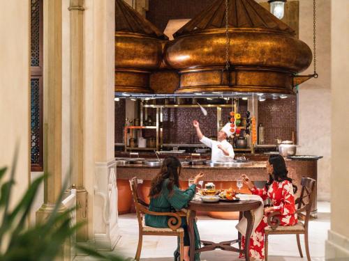 two women sitting at a table with a chef in the kitchen at Mövenpick Hotel Al Khobar in Al Khobar