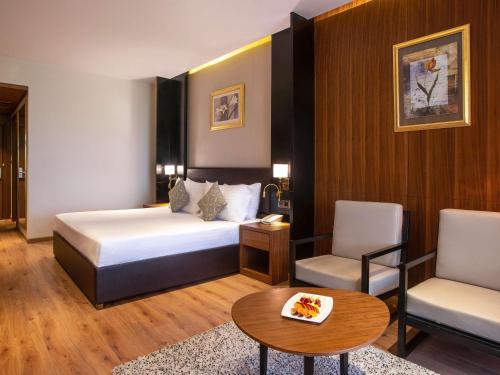 a hotel room with a bed and a chair and a table at Mövenpick Hotel Cairo - Media City in 6th Of October