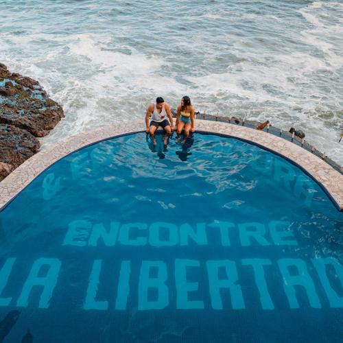 2 persone sedute in una piscina vicino all'oceano di Cadejo Brewing Company El Sunzal a Tamanique