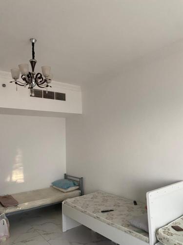 Camera bianca con 2 letti e un lampadario pendente. di عجمان هايتس ad Ajman