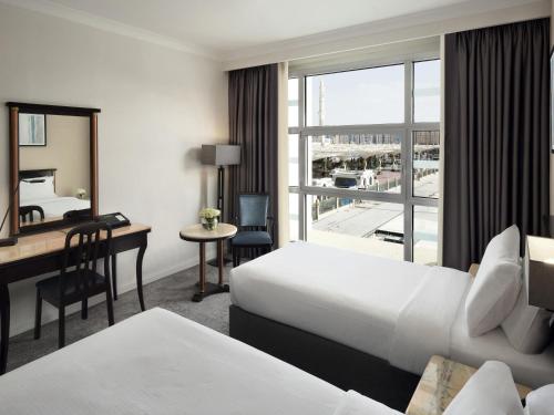 a hotel room with two beds and a desk and a window at Anwar Al Madinah Mövenpick in Al Madinah