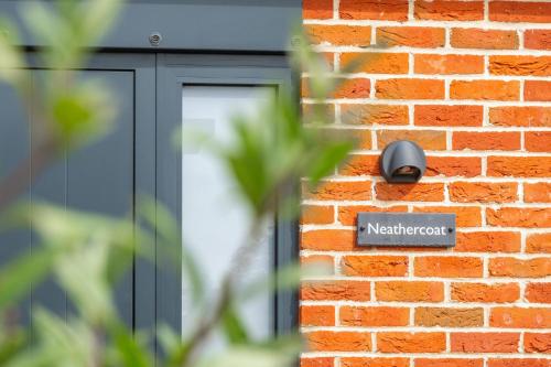 a sign on the side of a brick wall with a window at Neathercoat in Wells next the Sea