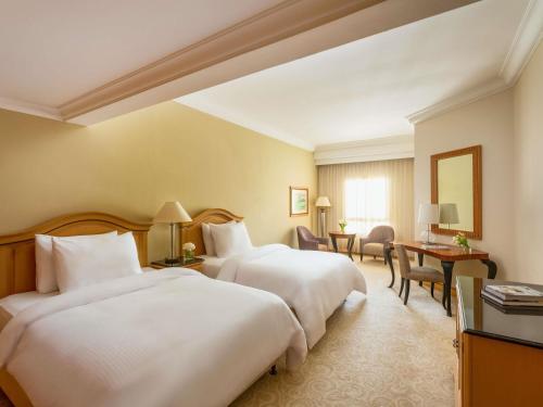 a hotel room with two beds and a desk at Mövenpick Hotel Doha in Doha