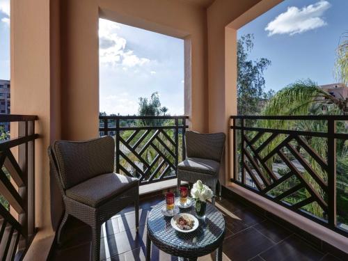 a balcony with two chairs and a table and two windows at Mövenpick Hotel Mansour Eddahbi Marrakech in Marrakech