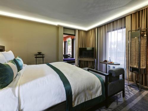 a hotel room with a large bed and a television at Mövenpick Hotel Mansour Eddahbi Marrakech in Marrakech