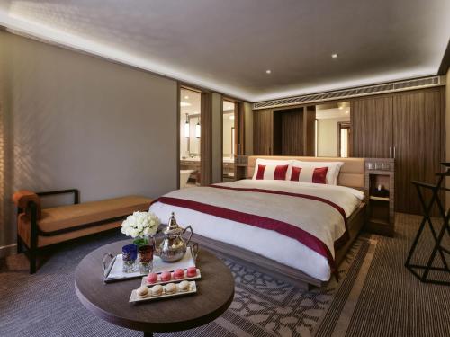 a hotel room with a large bed and a table at Mövenpick Hotel Mansour Eddahbi Marrakech in Marrakech