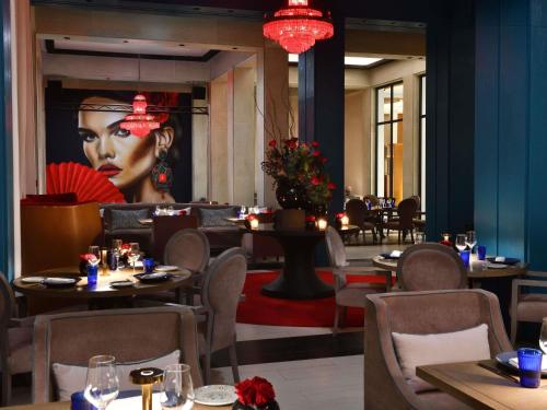 a restaurant with tables and a large painting of a woman at Mövenpick Hotel Mansour Eddahbi Marrakech in Marrakech