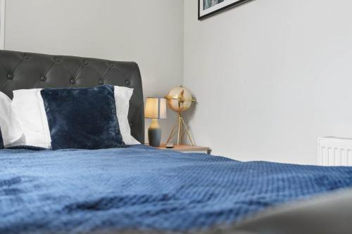a bed with a blue blanket and a lamp on a table at Lowestoft Seaside Escape by Eason Stays, Free Parking next to Sea Front in Oulton